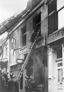 99444 Afbeelding van enkele brandweerlieden die op ladders bezig zijn met het nabluswerk aan het uitgebrande winkelpand ...